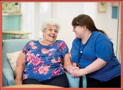 Image of a resident and member of staff laughing together and holding hands.